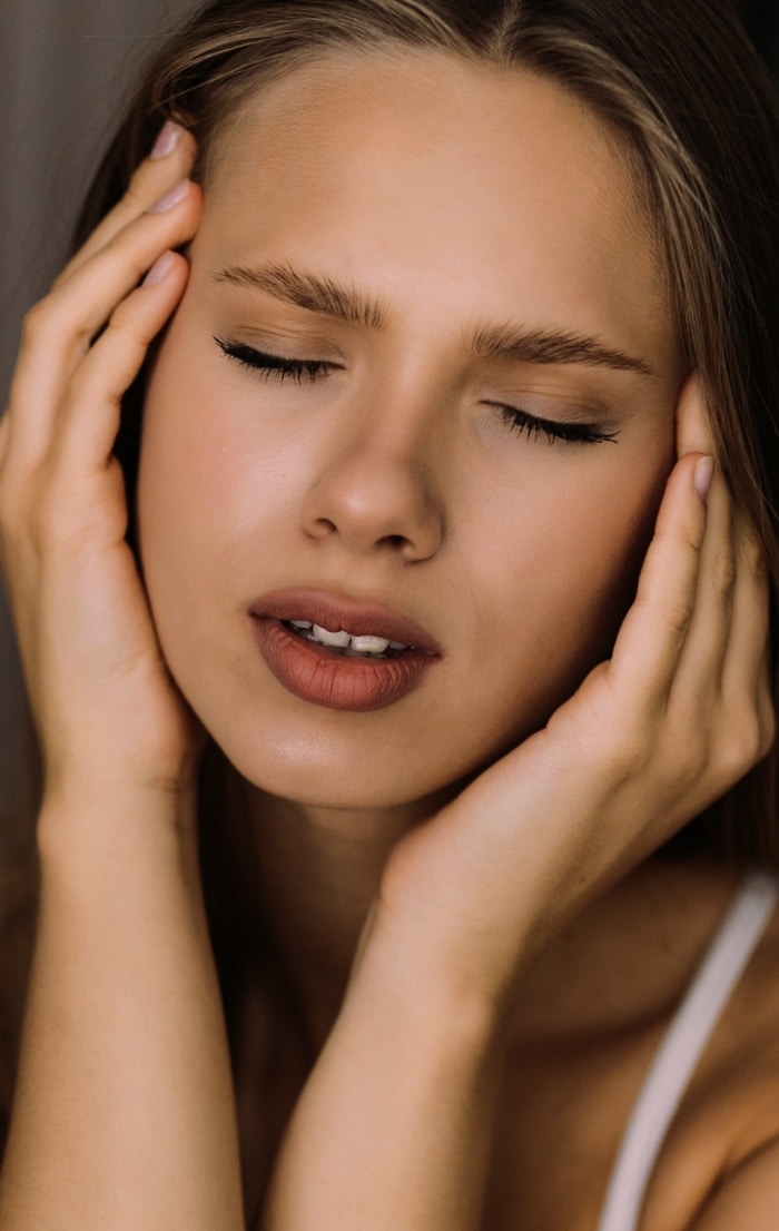 Photo d une jeune femme tenant sa tete avec ses mains les yeux fermes migraine | Dr Christophe Reinbold Lyon